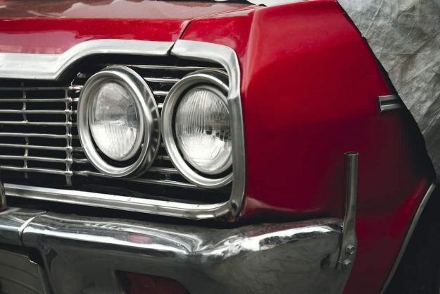 Classic American retro car under car case on the street. Bumper and headlight of red vintage car.